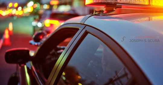 A police car at night alongside a road with emergency lights flashing.